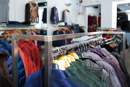 Various coats and blouses on hangers in clothing shop interiorの写真素材