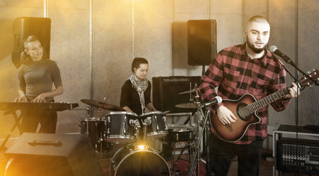 Rehearsal of music band. Happy cheerful  guy guitar player and singer practicing with band members...