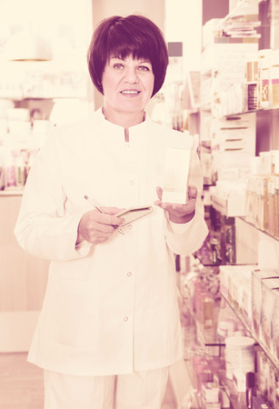 Portrait of cheerful  female druggist in white coat working in pharmacyの写真素材