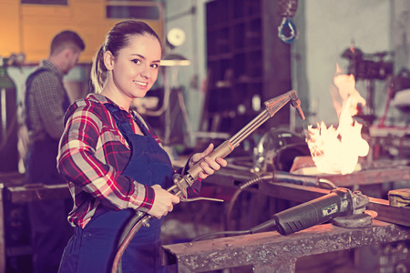 Smiling girl master is working with burner in workshopの写真素材