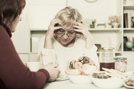 Upset mature lady having unpleasant talk with female friend at homeの写真素材