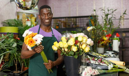 Smiling African-American man florist standing with fresh flowers in his floral shopの写真素材