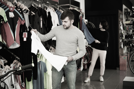 Young smiling couple choosing sport shirt in bicycle shopの写真素材