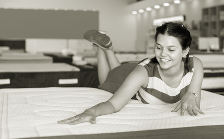 cheerful woman is lying on bed and testing mattress for relax in the storeの写真素材