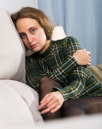 Portrait of sad girl sitting in living room at homeの写真素材