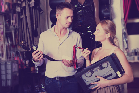 Positive seller consulting young customer with assortment of adult products in storeの写真素材