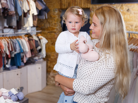 Young mother holding little daughter in her arms in baby clothing storeの写真素材
