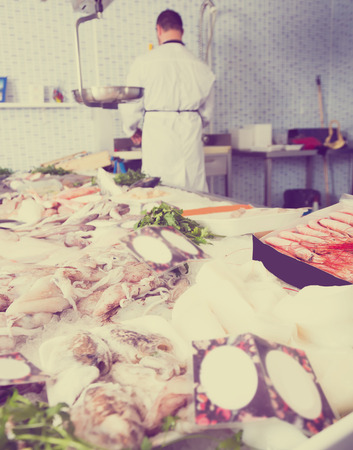 professional seller standing with his back to counter and cuts fish in the shopの写真素材