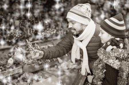 Smiling man with small daughter buying christmas decorations in market