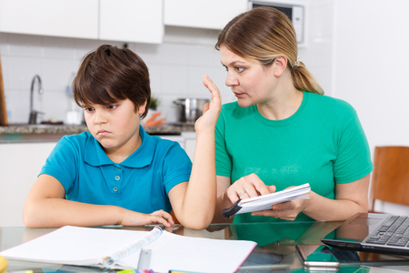 Annoyed mother helping son with homework sitting nearby at kitchen tableの写真素材