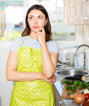 Young  girl housewife in apron looking tired at  kitchen at homeの写真素材