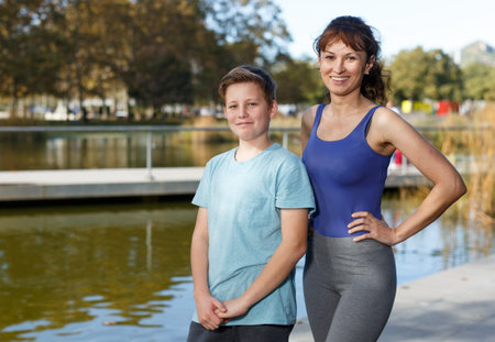 Portrait of happy woman with teen boy posing at autumn park, ready for workoutの写真素材