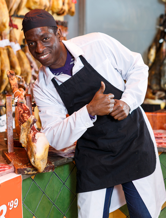 Successful butcher shop owner giving thumbs up, satisfied with quality of traditional spanish jamonの写真素材