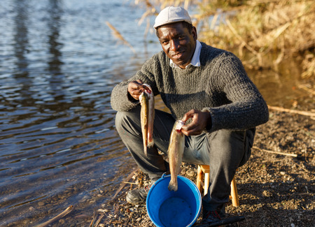 Mature African male fisherman holding fish in his handsの写真素材