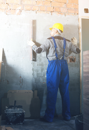 Male worker in helmet is measuring wall with level.の写真素材