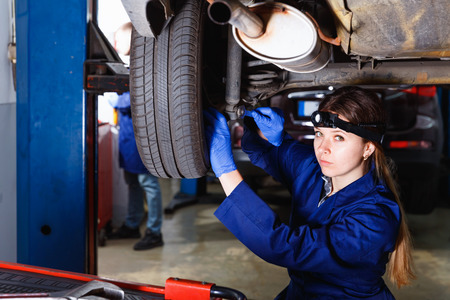 Young diligent pleasant woman master is repairing car in workshop.の写真素材