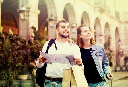 Portrait of happy young tourists with package walking with map at streetの写真素材