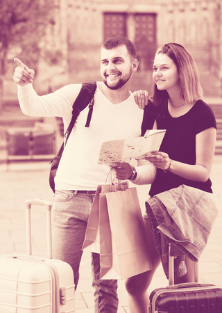 Couple of young tourists with baggage traveling with map at streetの写真素材