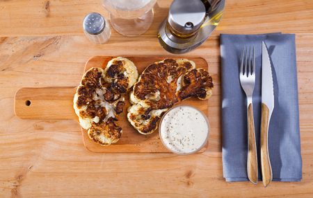 Top view of tasty grilled cauliflower steak with white sauce served on wooden board. Vegetarian foodの写真素材
