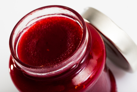 Closeup of tasty sweet raspberry jam in glass jar on white surface. Preserved berriesの写真素材