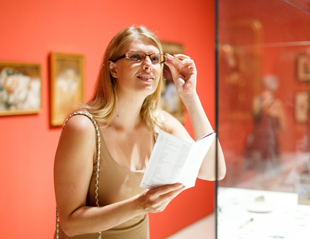 Positive woman with glasses visiting museum of arts with brochure in her handsの写真素材