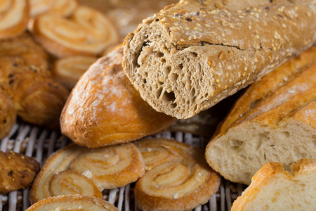 Closeup of cut wholegrain baguette with various bakery products on wicker matの写真素材