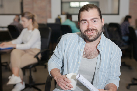 Portrait of cheerful male entrepreneur during daily work in modern office with coworkersの写真素材