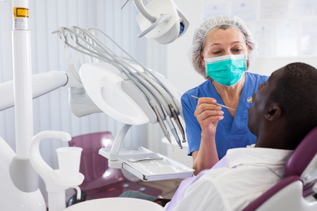 Dentist is treating male patient which is sitting in dental chairの写真素材