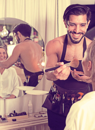 Cheerful man makeup artist applying cosmetics for femaleの写真素材