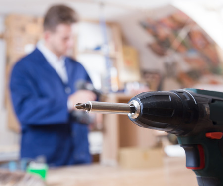 Young smiling guy using drilling machine at workshopの写真素材