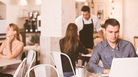 serious young man using laptop while waiting his order in modern cafeの写真素材
