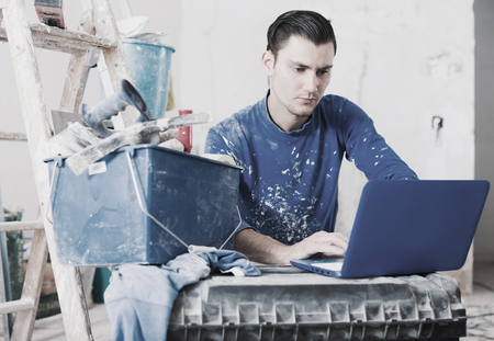 Serious builder handyman checking plan of house renovation on laptopの写真素材