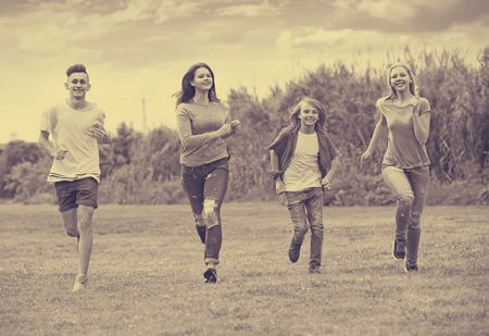 Four happy teenagers running together on green lawn in parkの写真素材
