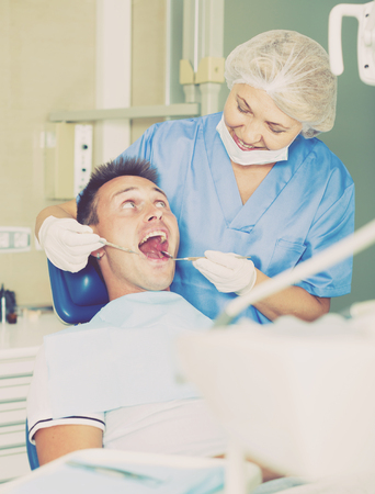 Female dentist treating young male patient in dental officeの写真素材