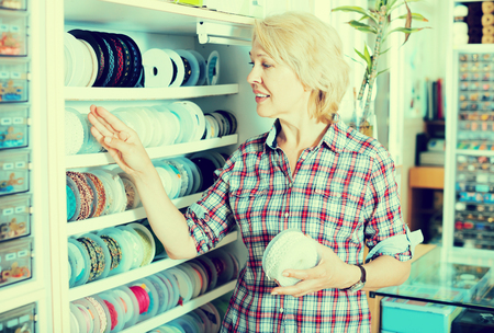 Positive woman customer selecting lacing or braid ribbon for her hobby in sewing storeの写真素材