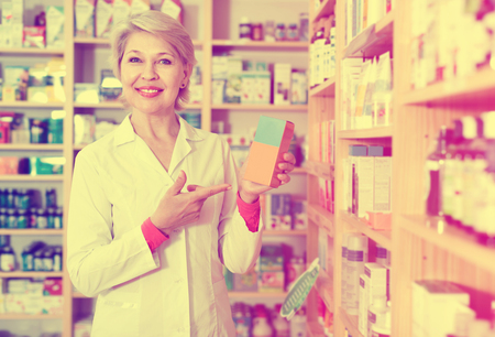 Glad cheerful positive smiling mature female seller suggesting useful skin care products in specialized shopの写真素材