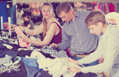 Smiling family of three with teenager choosing clothes a half-off sale in the  shopの写真素材