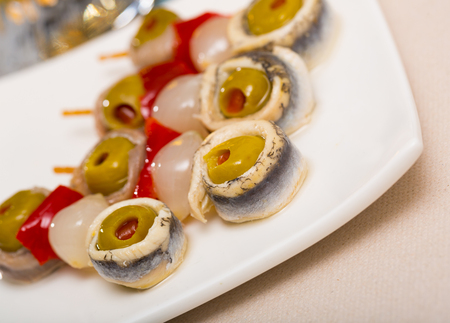 Appetizing pickled anchovy rolls with stuffed olives served on skewers with red pepper and onionの写真素材