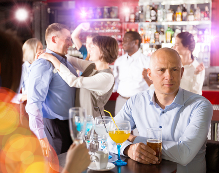 Bored man sitting at table among dancing colleagues at corporate partyの写真素材