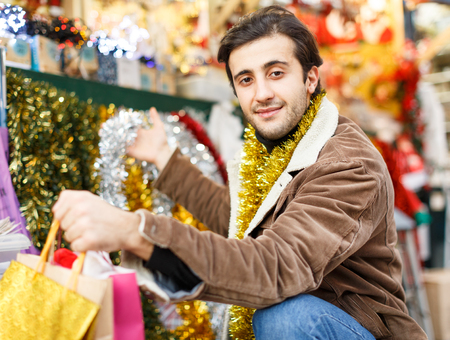 Smiling man with garland choosing decorations at Christmas marketの写真素材