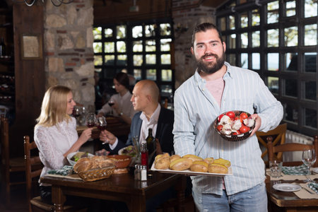 Positive male waiter welcoming guests to country restaurant