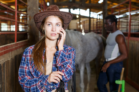 Young woman farmer worker using her mobile phone in stableの写真素材