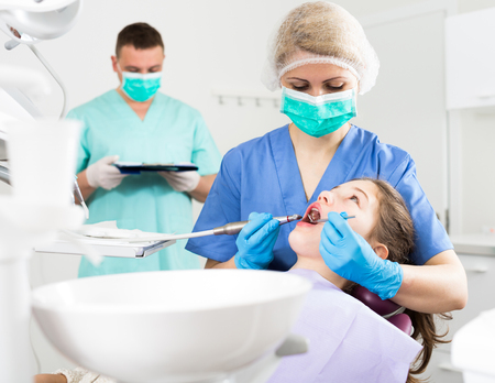 Female dentist treating teen girl patient in modern dental office with male assistantの写真素材