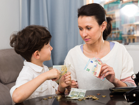 Smiling woman giving pocket money to her preteen son at homeの写真素材
