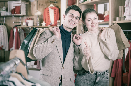 Smiling couple is satisfied of purchases and standing with package in the clothes store.の写真素材