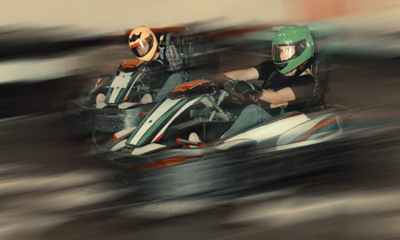 Young positive people in helmets driving go-kart cars in karting club