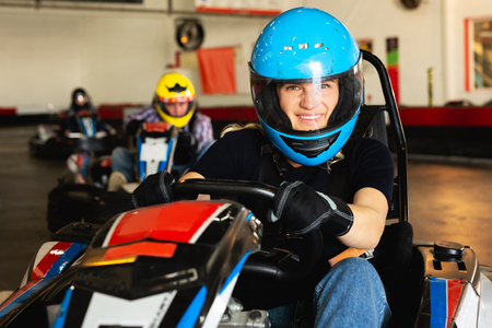 Young woman in helmet and other people driving cars for racing in sport club indoorの写真素材