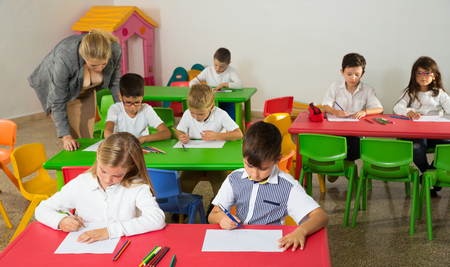 Female teacher helping schoolchildren doing their task in classroomの写真素材