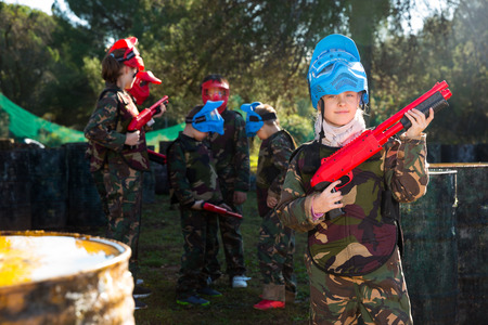 portrait of little girl paintball player in camouflage standing with gun before playing outdoorsの写真素材