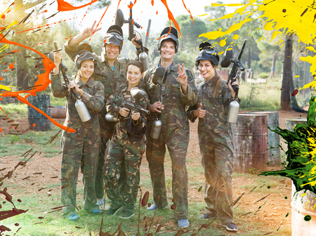 Happy group of paintball players in camouflage standing with guns on paintball playing field outdoorsの写真素材